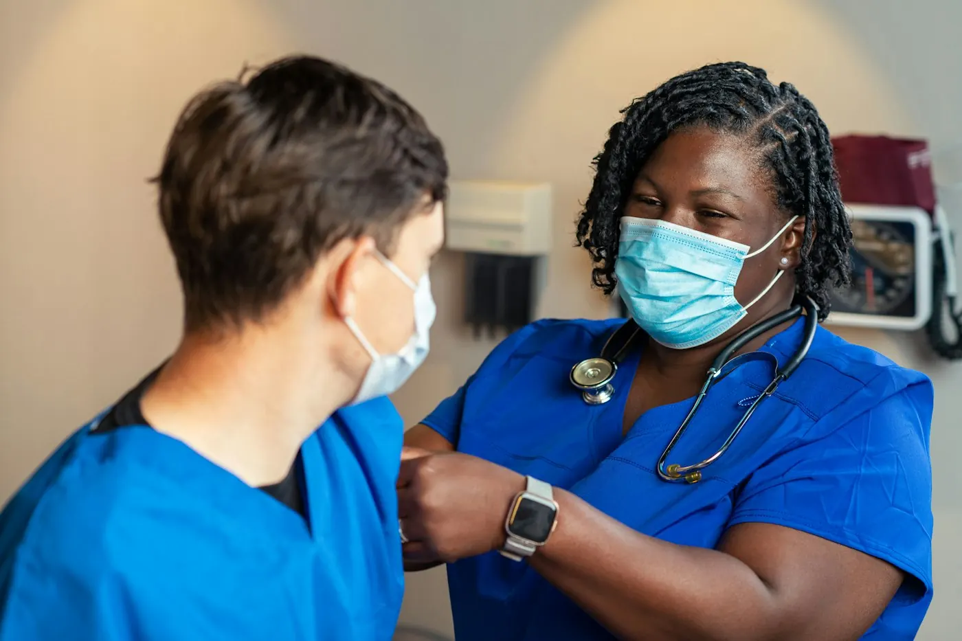 A clinician in scrubs with a stethoscope attending to a colleague