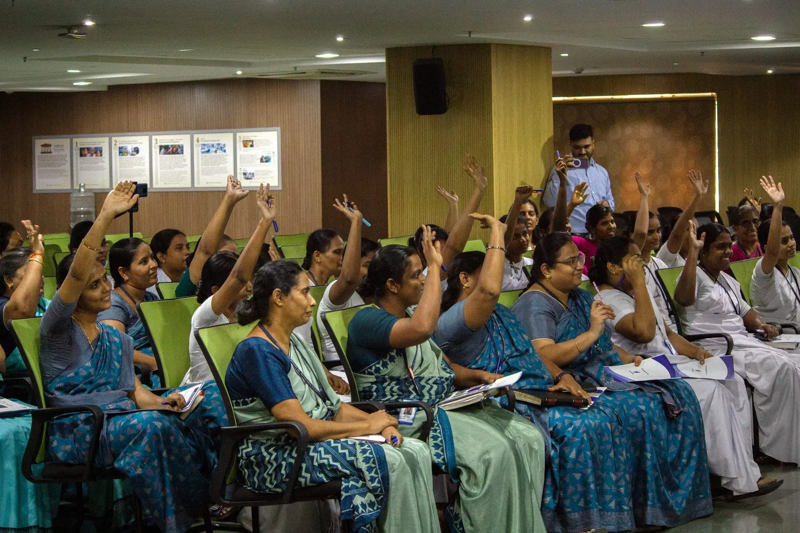A classroom of healthcare staff raising their hands during a facilitated session